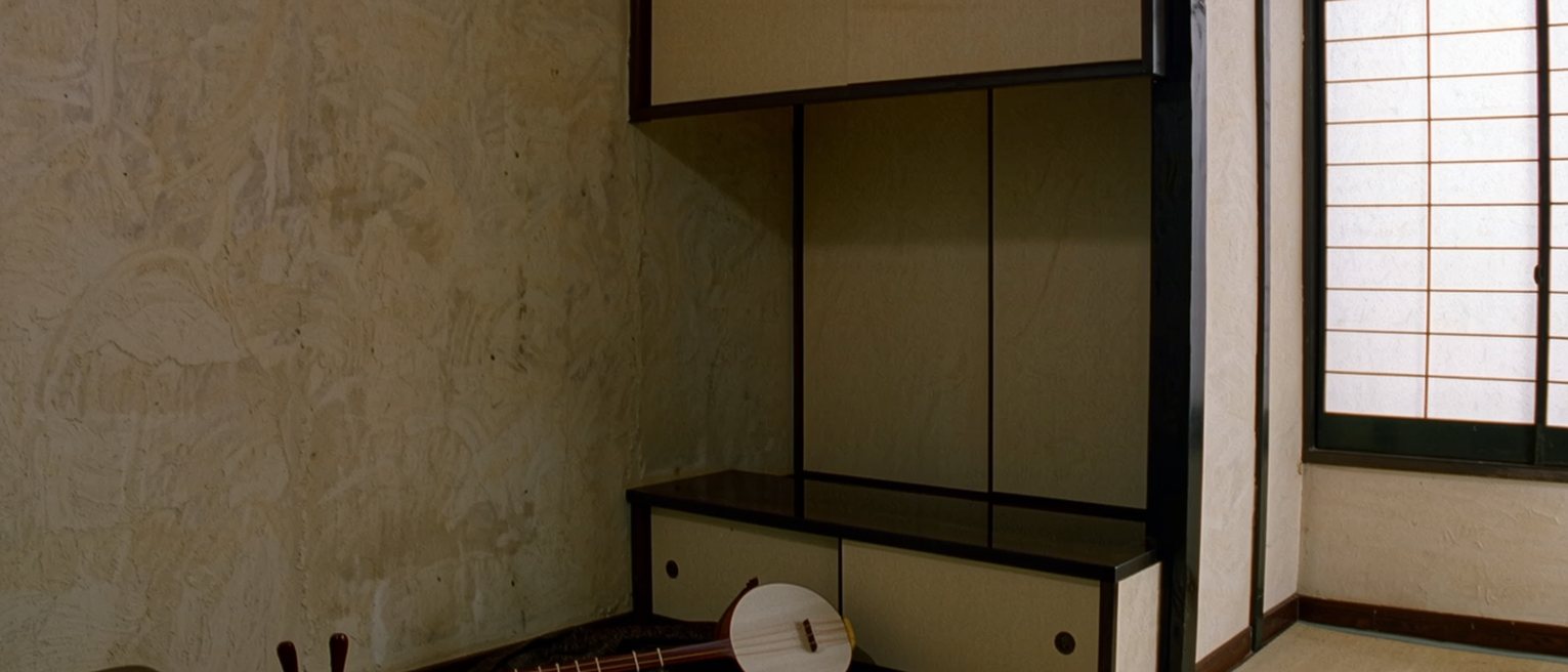 a tatami room seen close with a shamisen in its cloth cover laid on the floor beside a low table with a cup of sake untouched, the alcove close behind and the shoji soft beyond