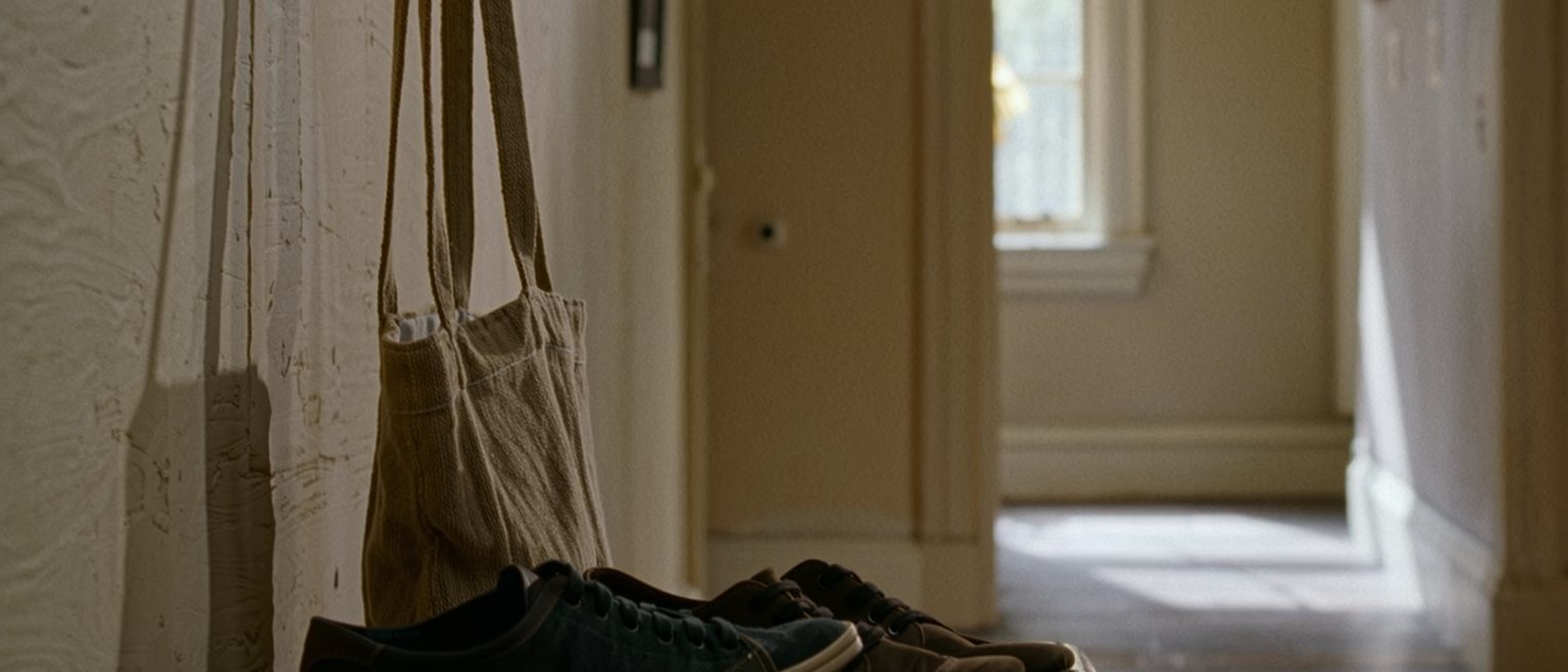 a hall seen close with a canvas bag packed and standing ready on the bench beside a folded card and a set of keys, a pair of low shoes below, the door soft beyond