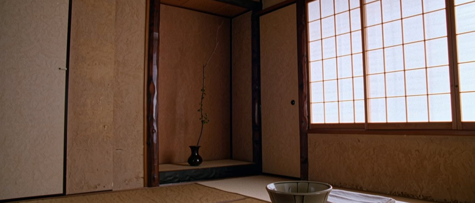 a tatami room seen close with a single tea bowl on a low table and a folded cloth beside it, the alcove with one branch in a vase close behind and the shoji soft beyond