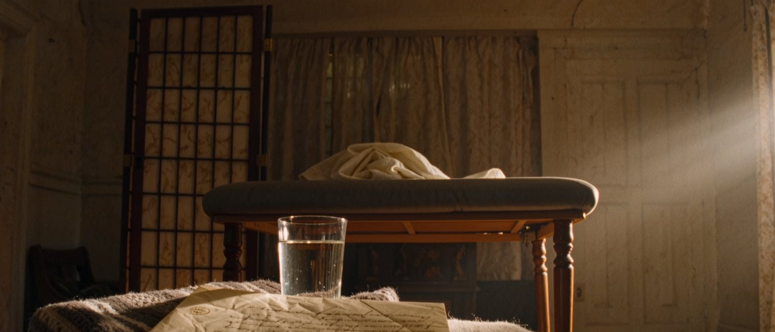 a quiet room seen close with a written agreement in its envelope on a low table, a glass of water and a folded blanket, the padded table with its sheet turned down close behind and the paper screen soft beyond