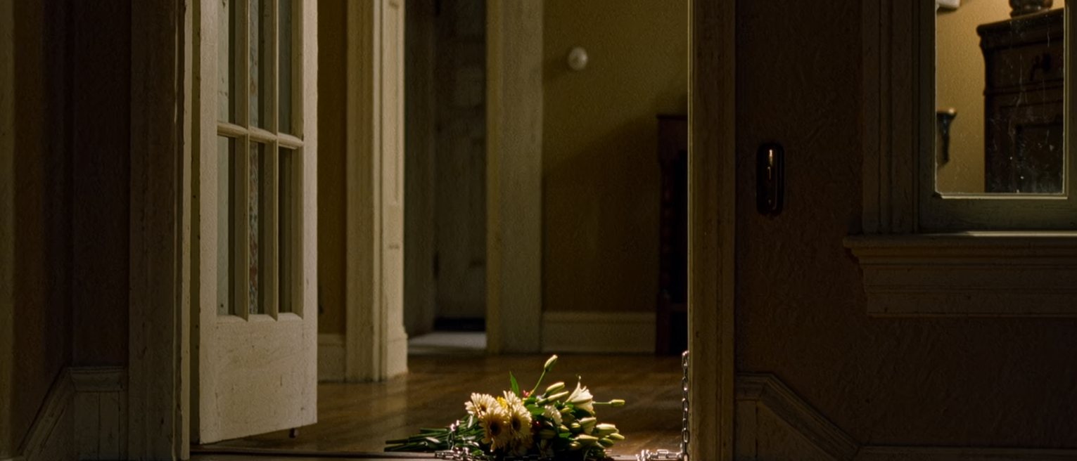 a front door with the chain on and a bunch of flowers left outside on the step, seen through the gap from inside, coats on the hooks and the hall lamp close beside the door