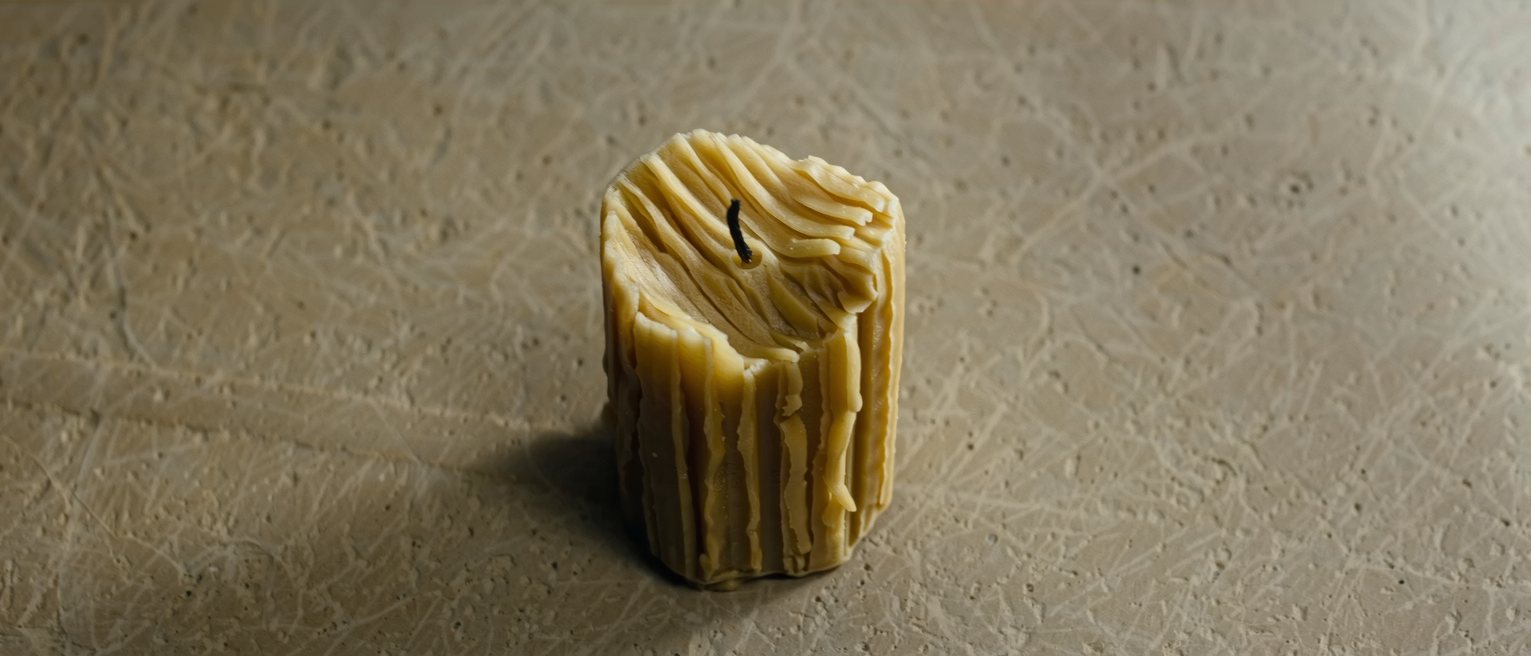 a beeswax candle burned down unevenly on one side, the wax cooled mid-run