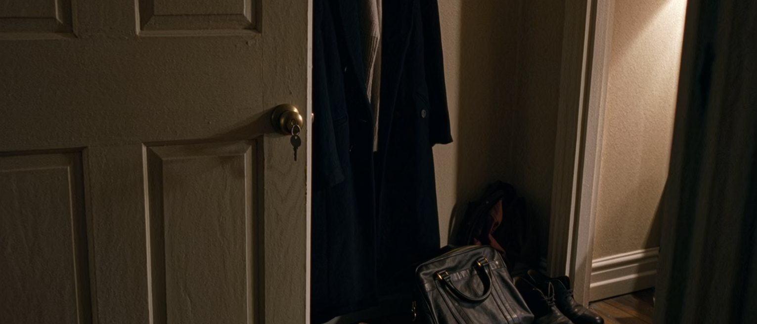 a bedroom door seen from inside with the key turned in the lock and a coat, a bag and a pair of shoes ready beside it