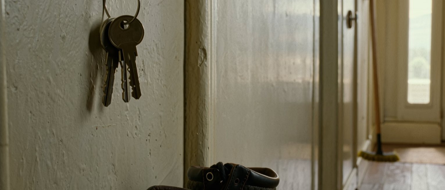 a hall with two sets of keys on one hook and, beneath them, a pair of walking boots each with mud still on them from the same walk