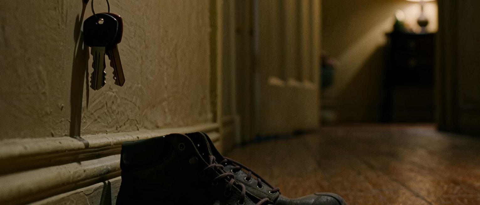 a hall with two sets of keys on one hook and, beneath them, a pair of walking boots each with mud still on them from the same walk