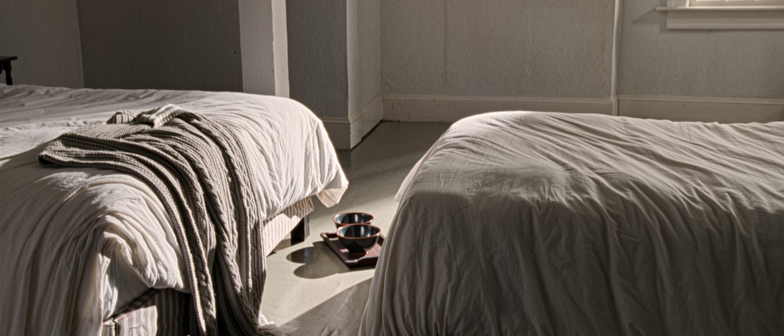 a bedroom with the covers thrown back on both sides and a tray with two empty bowls on the floor, nothing tidied