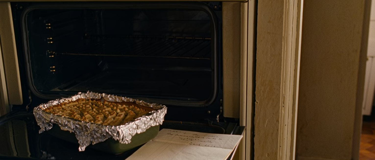 a kitchen counter where a casserole dish brought round from next door still sits covered in foil beside a folded note, untouched, the oven empty behind it
