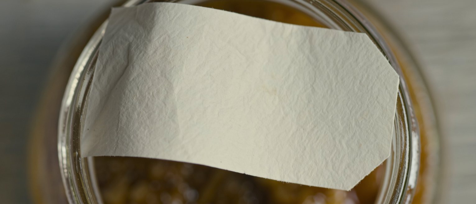 a blank unprinted gummed label half lifted from a glass jar, the adhesive giving way