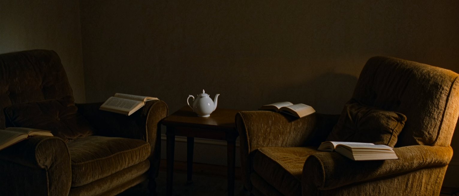 a sitting room with two armchairs, a book open face down on the arm of each, and one pot of tea on the table between them
