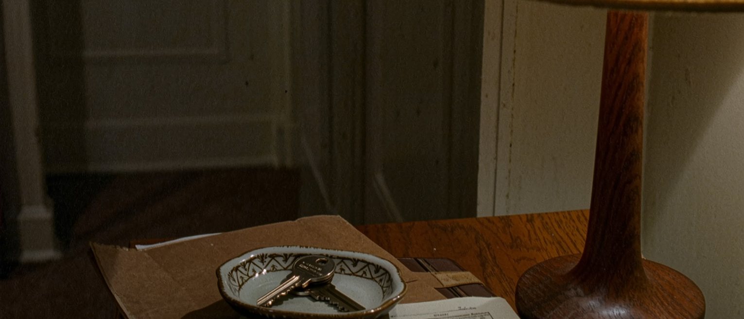 a bedroom seen close with two sets of keys in a dish on the bedside table, a copy of the penal code with a page flagged, a lease in a folder and the lamp close behind
