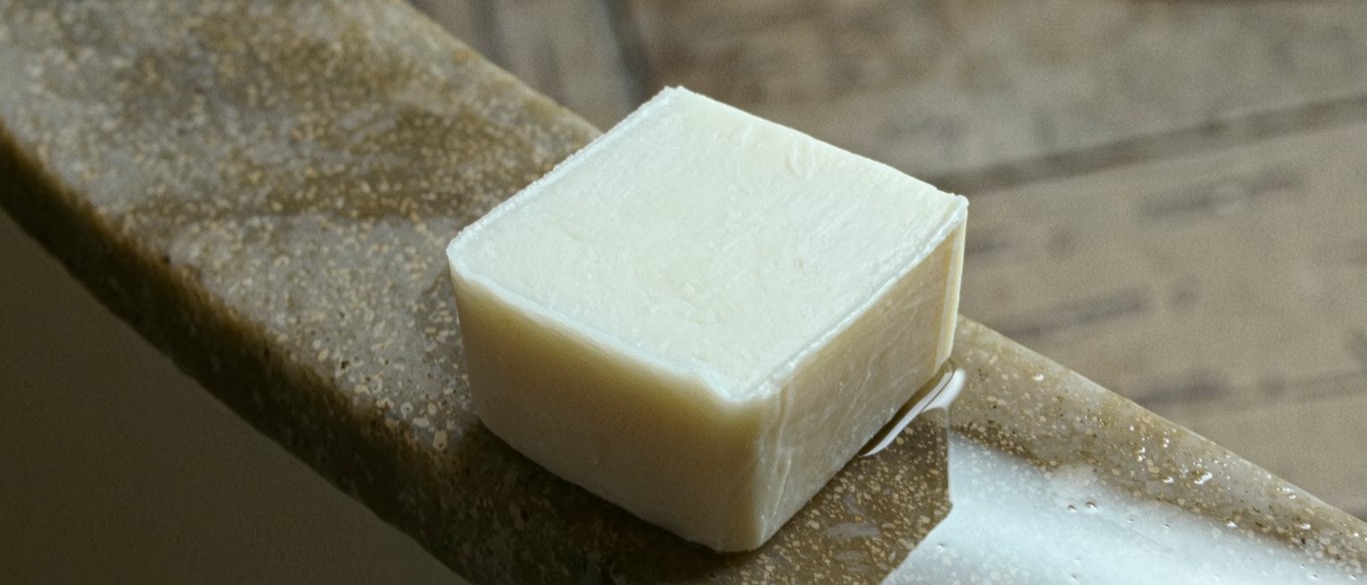 a plain unperfumed cake of soap, unwrapped and square-edged and never used, resting on a wet stone ledge