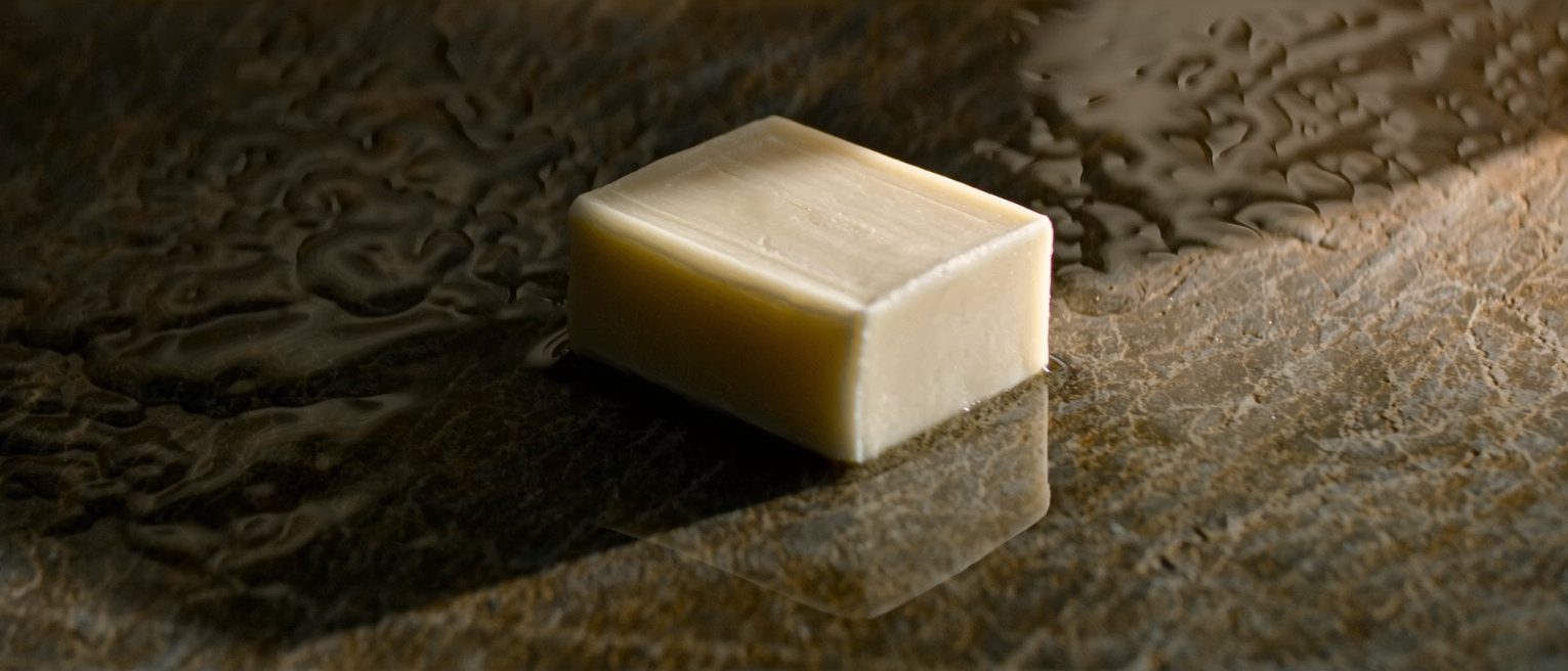 a plain unperfumed cake of soap, unwrapped and square-edged and never used, resting on a wet stone ledge