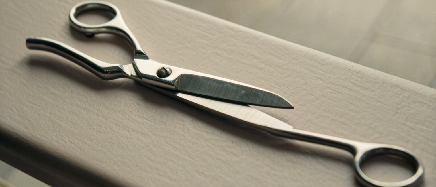 a pair of long tailor's shears laid open on a bare hardwood workbench, the blades bright along the cutting edge