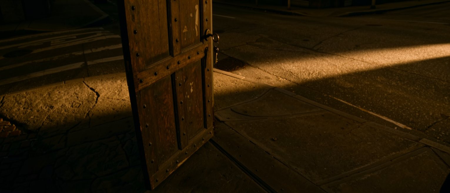 a studded wooden door standing open onto a lit street