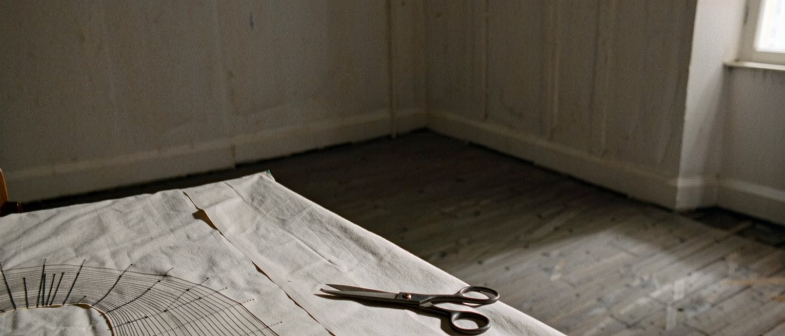 a tailor's table with a paper pattern pinned out on cloth and the shears set down beside it