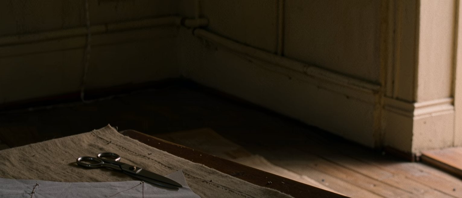a tailor's table with a paper pattern pinned out on cloth and the shears set down beside it