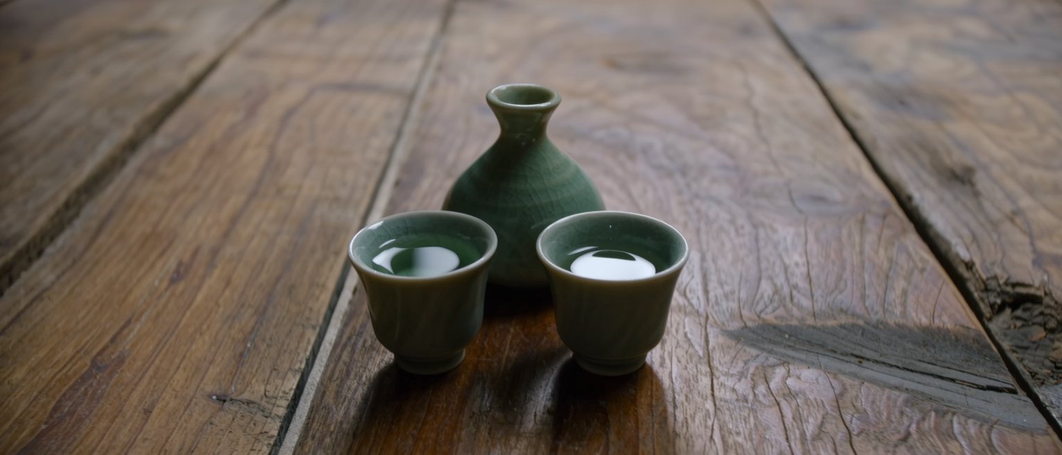 two small sake cups and one flask set down together on a worn wooden counter