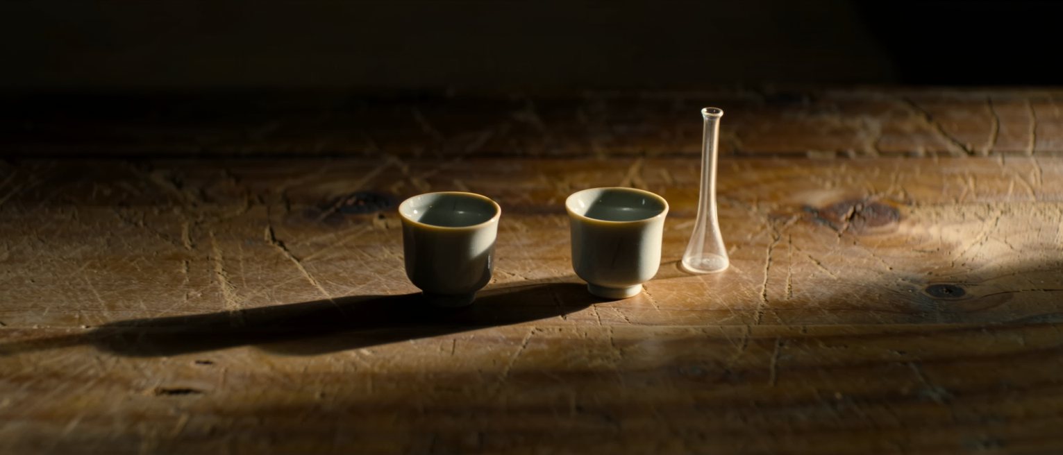 two small sake cups and one flask set down together on a worn wooden counter