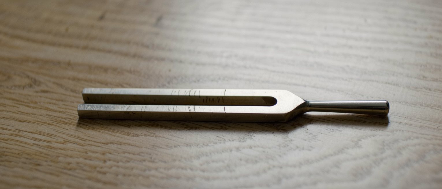 a steel tuning fork resting on a wooden soundboard, still after being struck