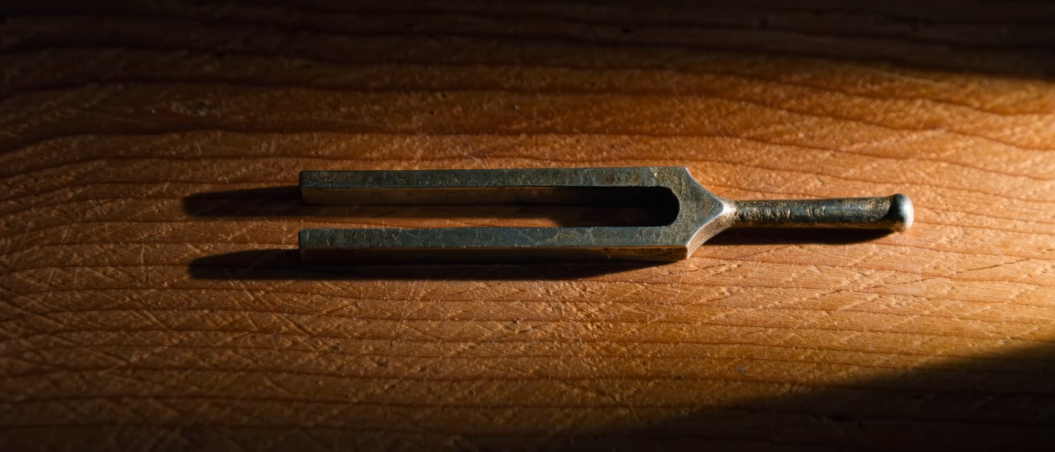a steel tuning fork resting on a wooden soundboard, still after being struck