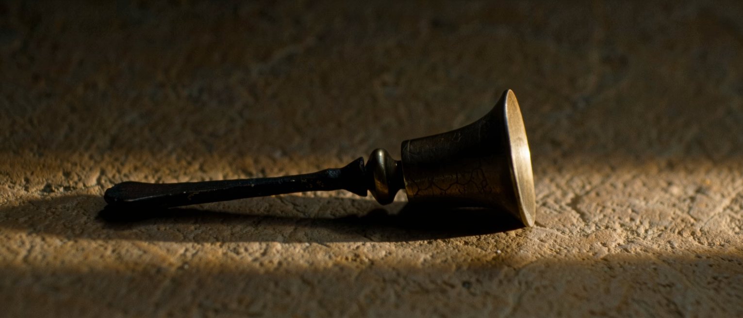 a small bronze bell with its striker laid down beside it, neither touching