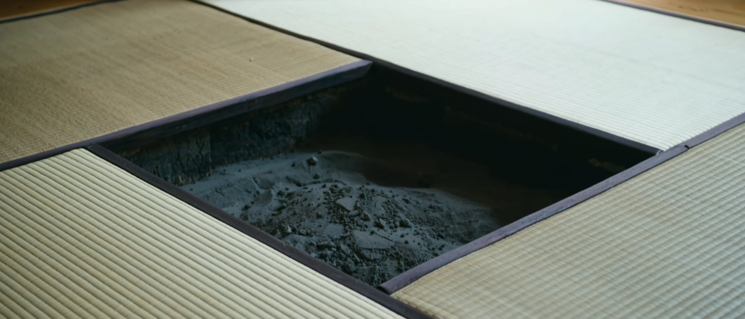 a sunken hearth cut square into tatami matting, the ash inside it raked level