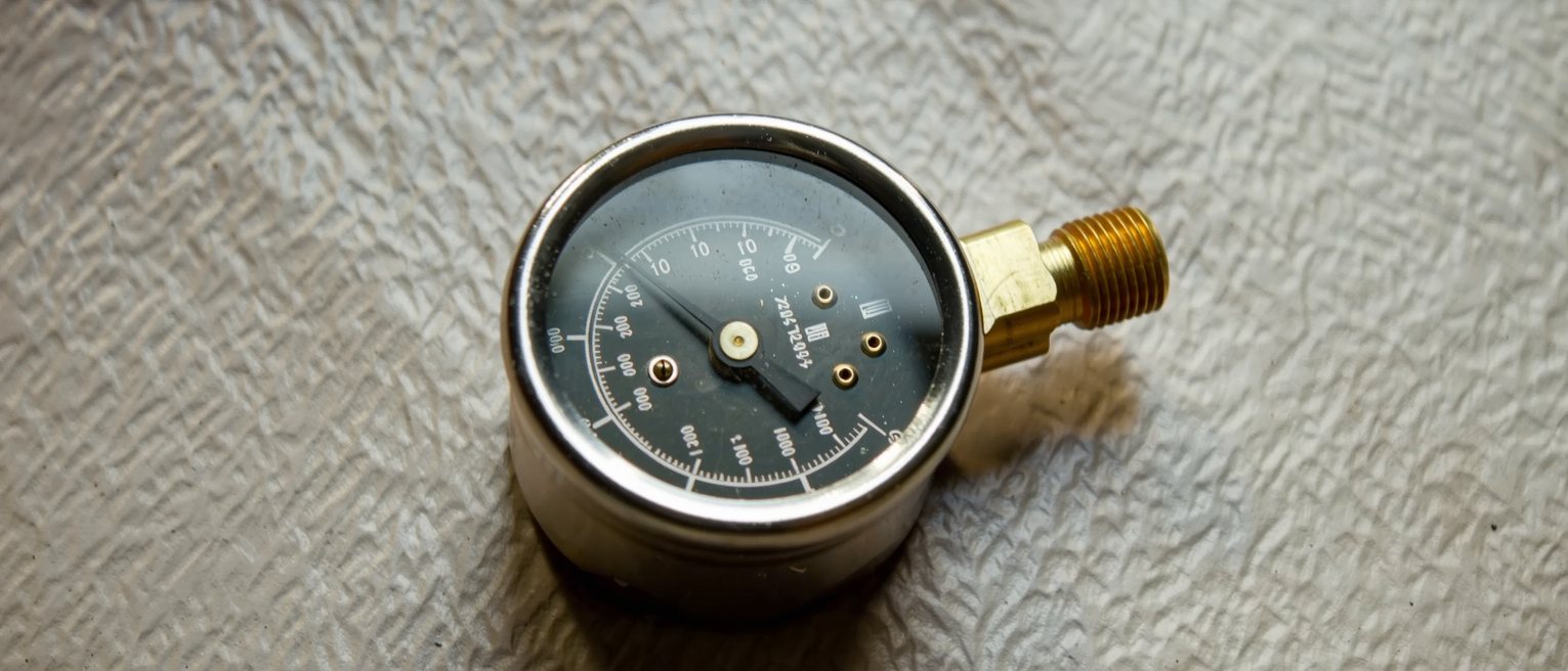 a brass pressure gauge with its needle resting flat at zero, the glass dusty