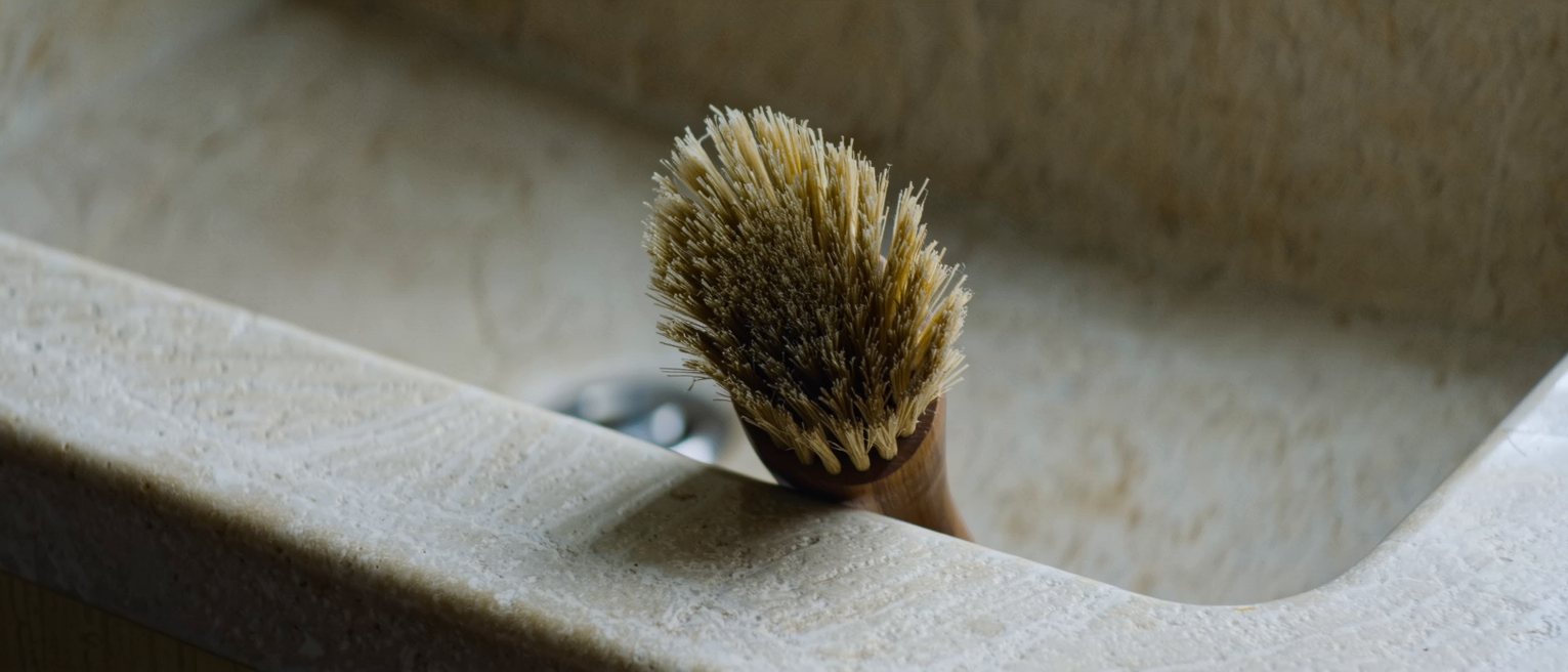 a scrubbing brush worn down on one side, standing on the edge of a stone sink