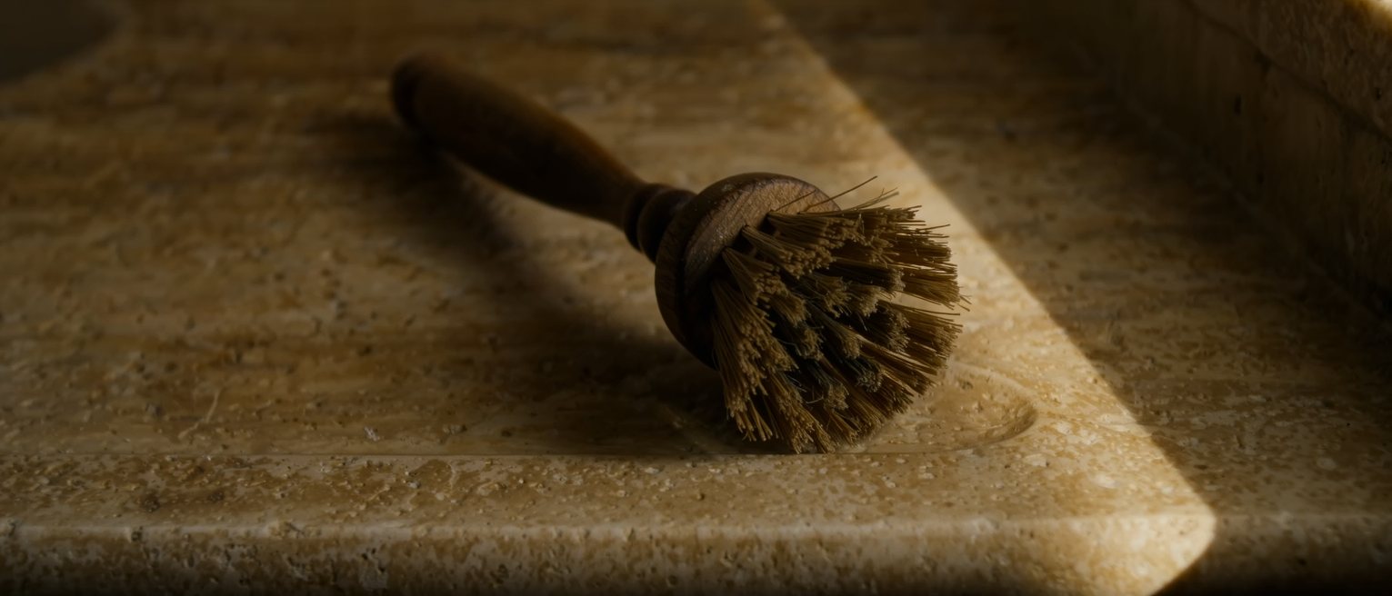 a scrubbing brush worn down on one side, standing on the edge of a stone sink