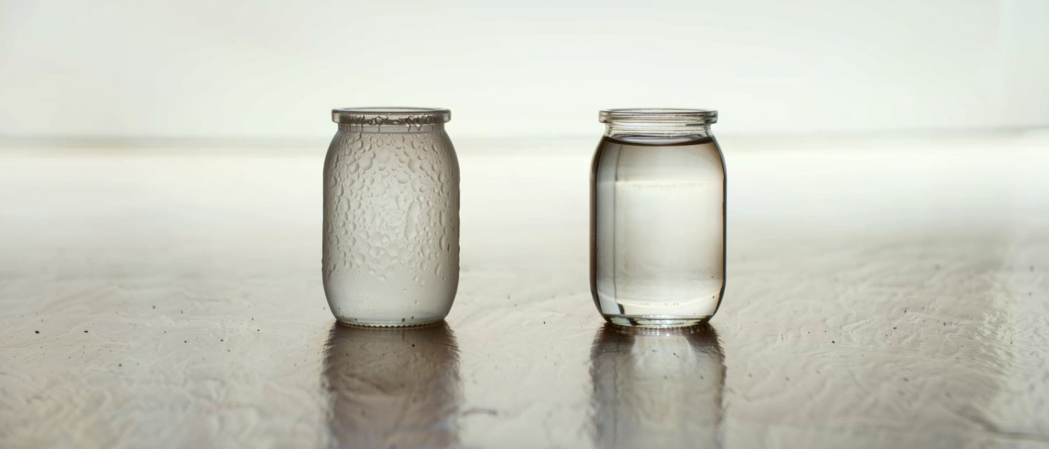 two identical glass jars holding the same amount of water at different temperatures, one fogged and one clear
