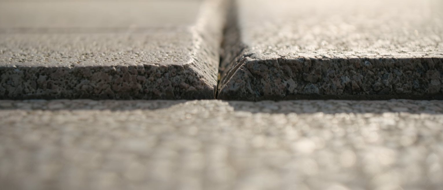 two granite kerbstones meeting along one straight joint, the left block weathered smooth and the right still sharp-arrised