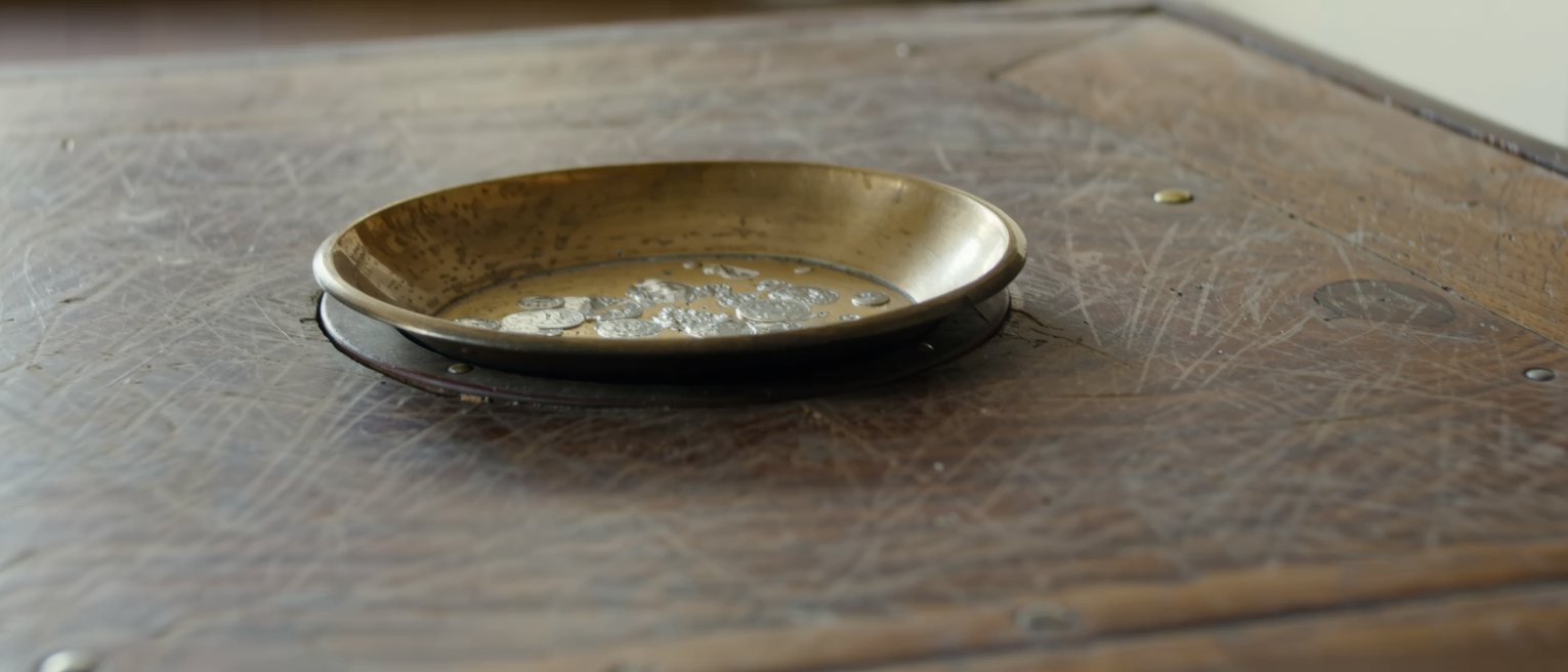a worn wooden counter top with a shallow brass-lined tray let into it, the lacquer rubbed through where coins have been set down