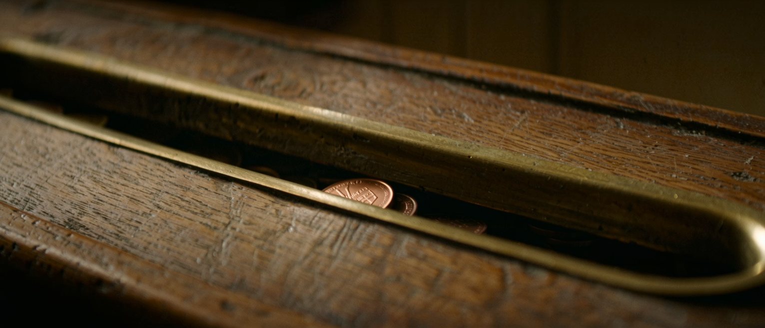 a worn wooden counter top with a shallow brass-lined tray let into it, the lacquer rubbed through where coins have been set down