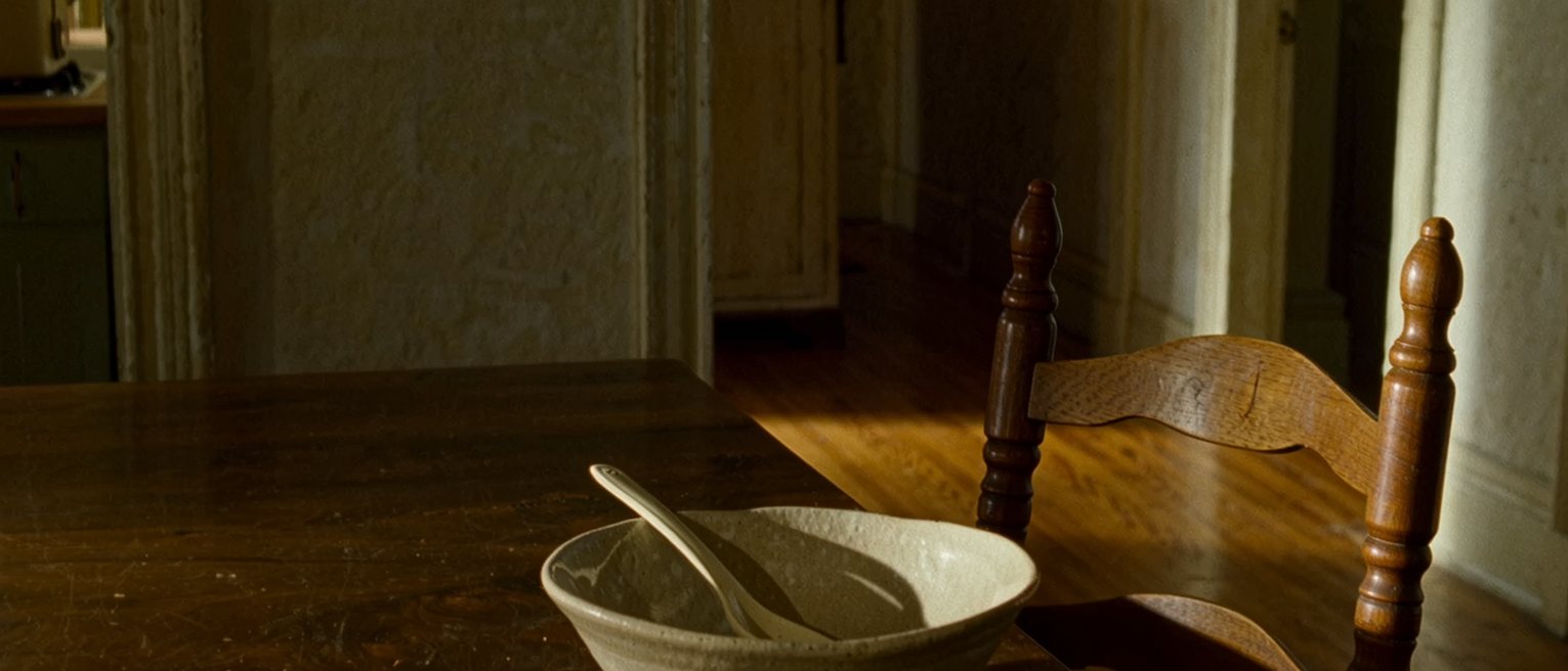 a kitchen on a Tuesday: the same bowl, the same spoon, the same chair, the post on the table, everything known