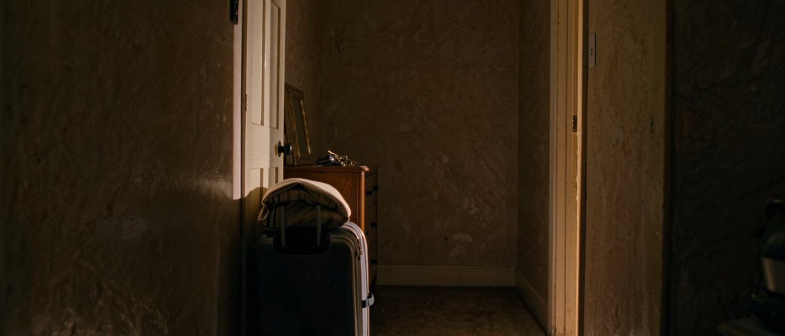 a hall seen close with a suitcase packed by the door, two small pairs of shoes side by side on the mat and a set of keys on the console, the door soft behind