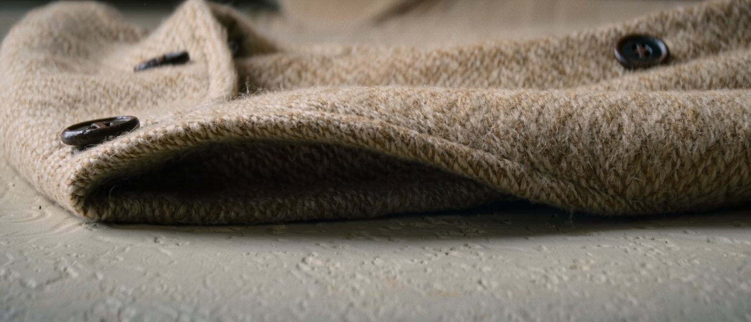 the turned-up collar and shoulder of a heavy wool overcoat hanging on an iron peg, the lapels and the weave of the wool clearly visible