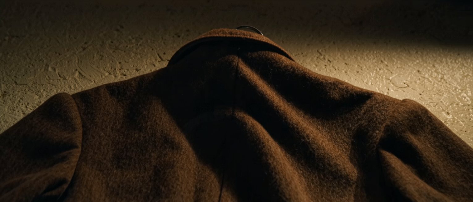 the turned-up collar and shoulder of a heavy wool overcoat hanging on an iron peg, the lapels and the weave of the wool clearly visible