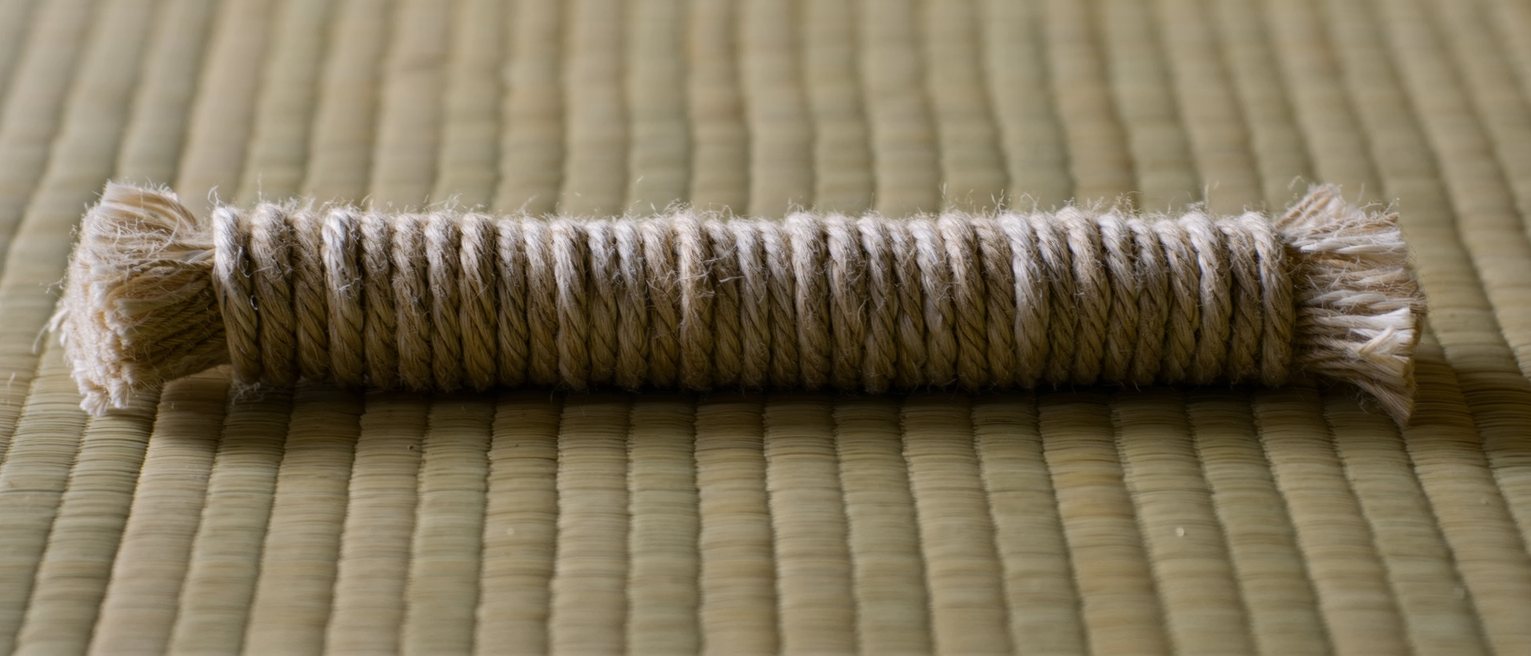 a coil of dyed jute rope laid in flat concentric turns on a tatami mat, the fibres slightly furred