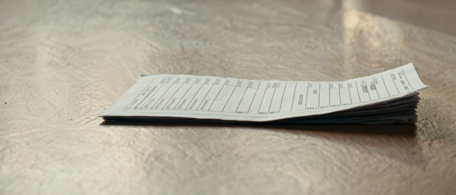 an itemised paper account folded once and left face down on a counter, the corner curling up