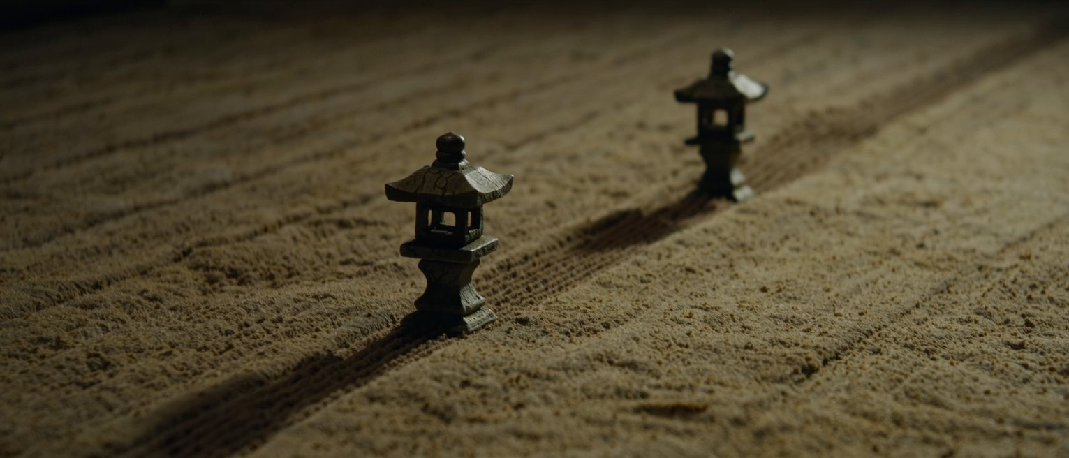 two stone lanterns set far apart along a path, the ground between them raked