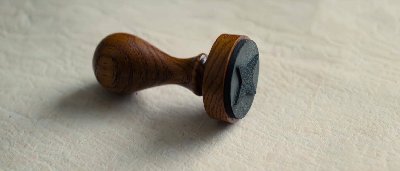 a wooden-handled rubber stamp resting on its ink pad, the rubber pad uncut and blank