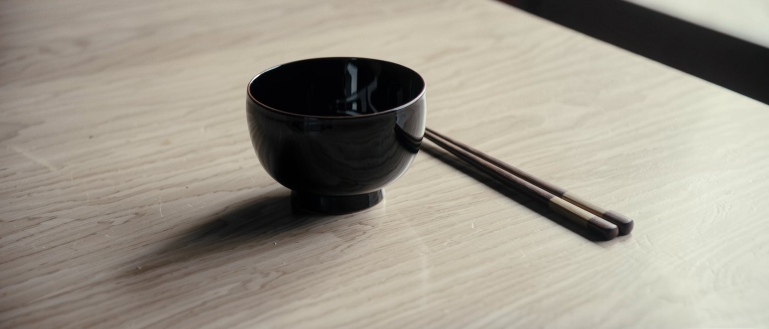 one lacquer bowl and one pair of chopsticks set down on a long bare table