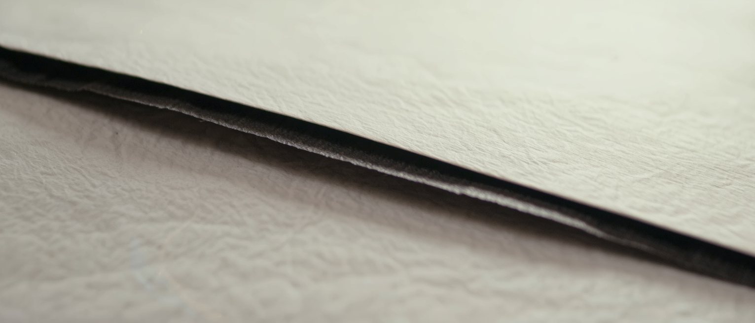 a sheet of carbon paper lifted from between two blank forms, the carbon side dark and slightly creased