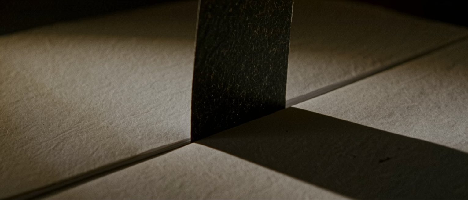 a sheet of carbon paper lifted from between two blank forms, the carbon side dark and slightly creased