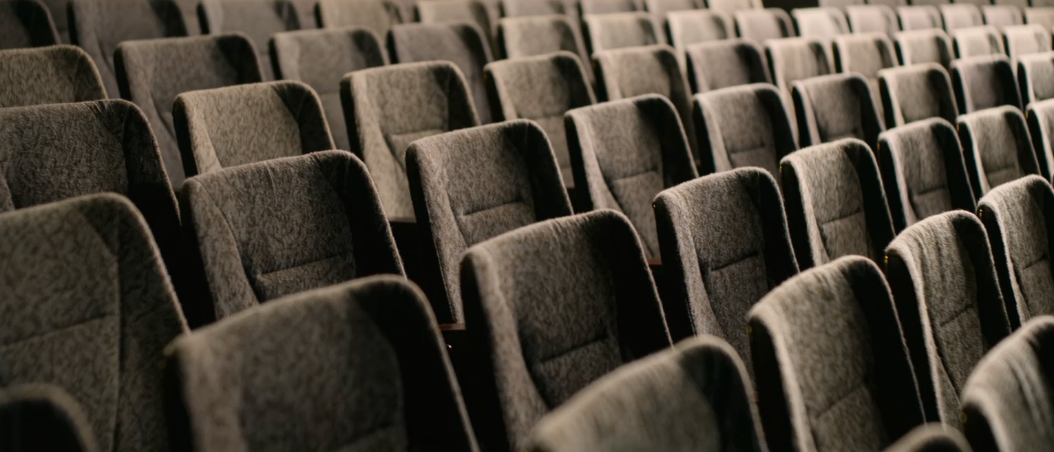 a row of empty seats in a dark auditorium, lit only along their backs