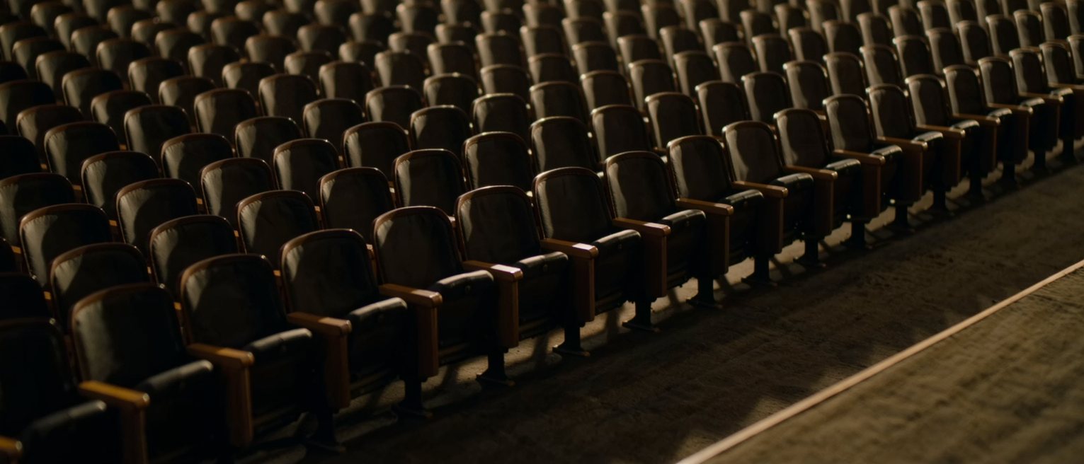 a row of empty seats in a dark auditorium, lit only along their backs
