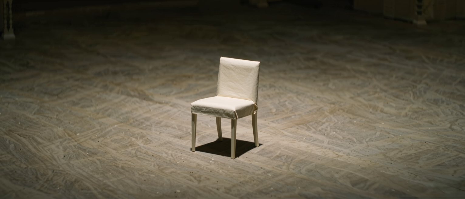 a single chair set on a bare stage with the house lights down