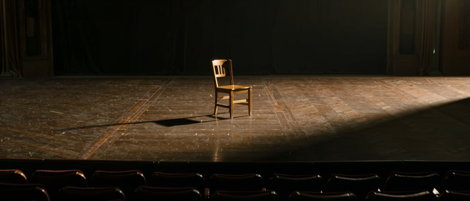 a single chair set on a bare stage with the house lights down