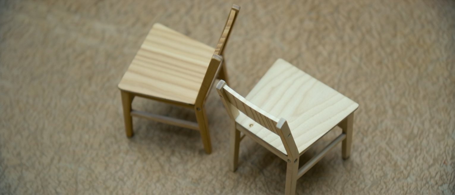 an empty chair of pale wood turned slightly toward another, both seats unworn on one side