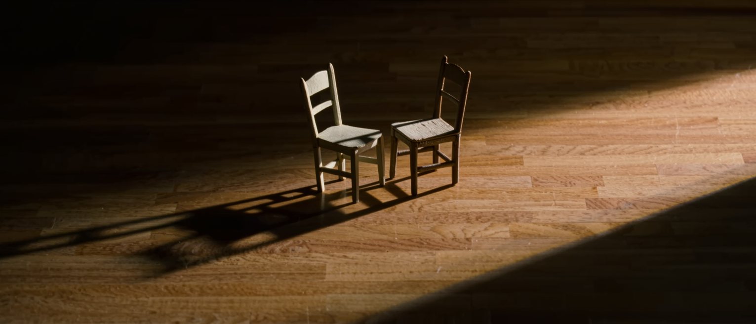 an empty chair of pale wood turned slightly toward another, both seats unworn on one side